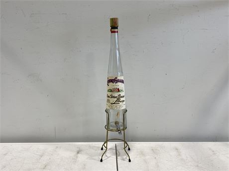 VINTAGE LIQUOR BOTTLE IN BRASS STAND (28” TALL)